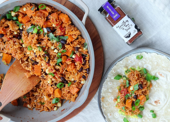 a skillet with burrito filling which includes Mexican rice with sweet potatoes with a burrito wrap on the side and a bottle of Something to Taco Bout spice blend.  