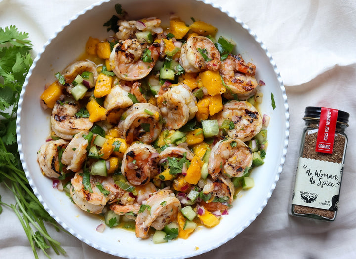 Grilled jerk shrimp over mango, cucumber, and cilantro salsa in a white bowl, beside a jar of Healthy On You Jamaican Jerk spice blend.