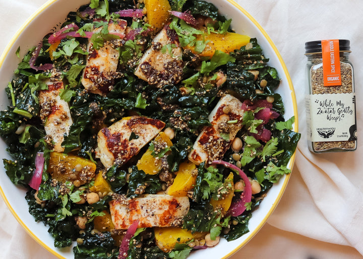 Yellow beet and kale salad with seared halloumi, chickpeas, and pickled onions, beside a jar of Healthy On You Za'atar spice blend.