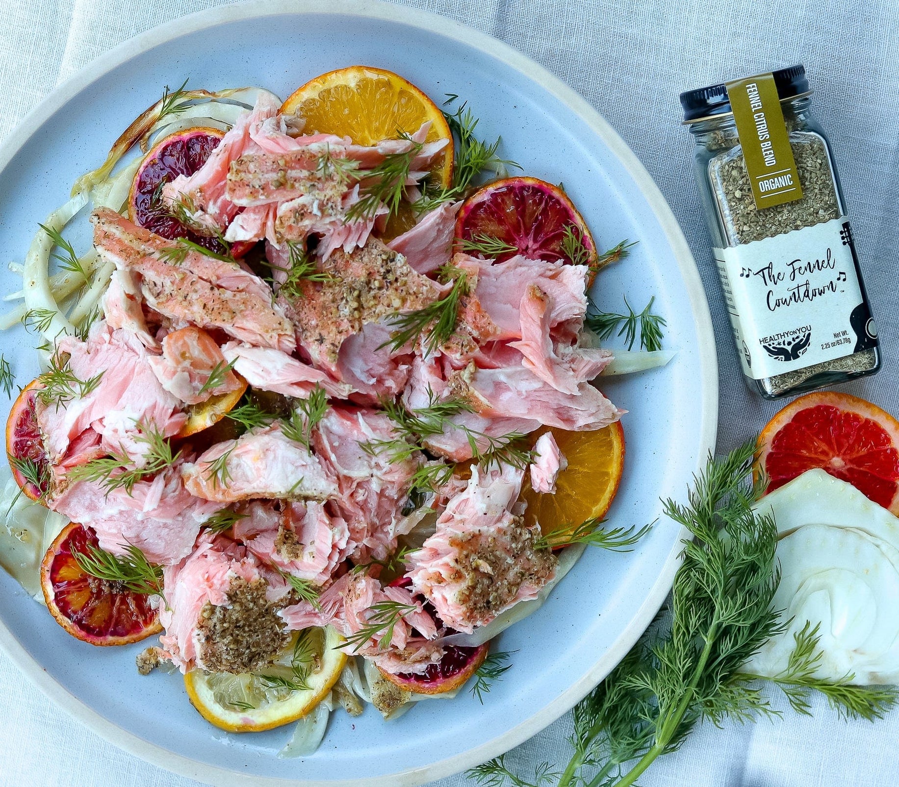 Salmon salad with blood oranges and herbs on a plate, with a bottle of seasoning in the background.